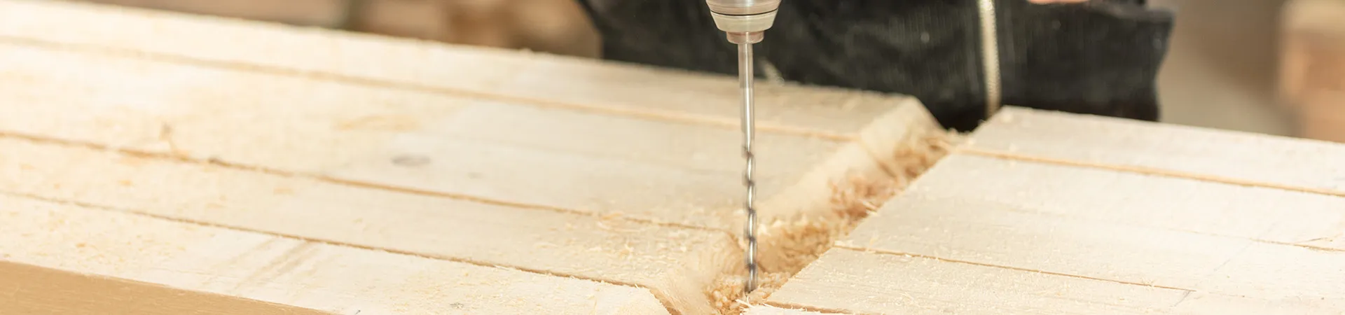 Bohrer durchdringt ein Holzbrett, Sägespäne entstehen.