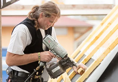 Handwerker befestigt Dachlattung mit Nagelgerät.